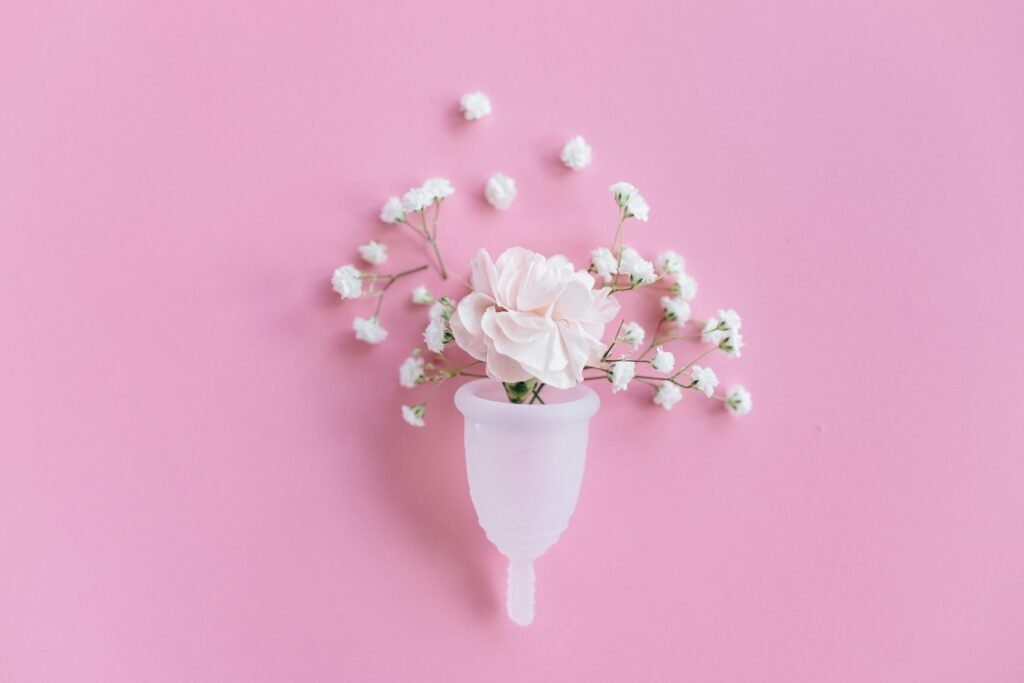 A menstrual cup filled with delicate flowers on a pink background, symbolizing feminine care and eco-friendly solutions.