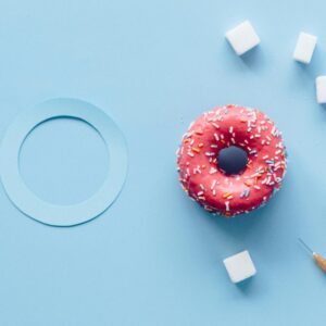 Flat lay of a pink donut, sugar cubes, and syringe on a blue background symbolizing diabetes awareness.
