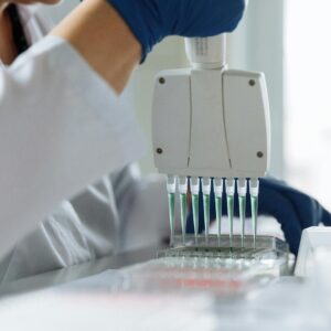 A scientist wearing a lab coat uses a multichannel pipette for liquid handling in a lab setting.