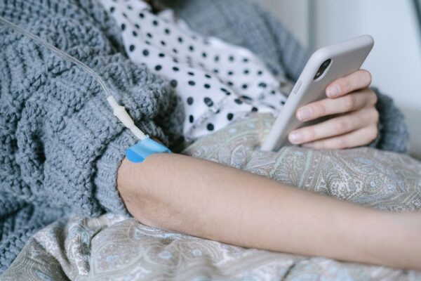 A woman receiving intravenous therapy for cancer treatment while using her phone, symbolizing connection and hope.