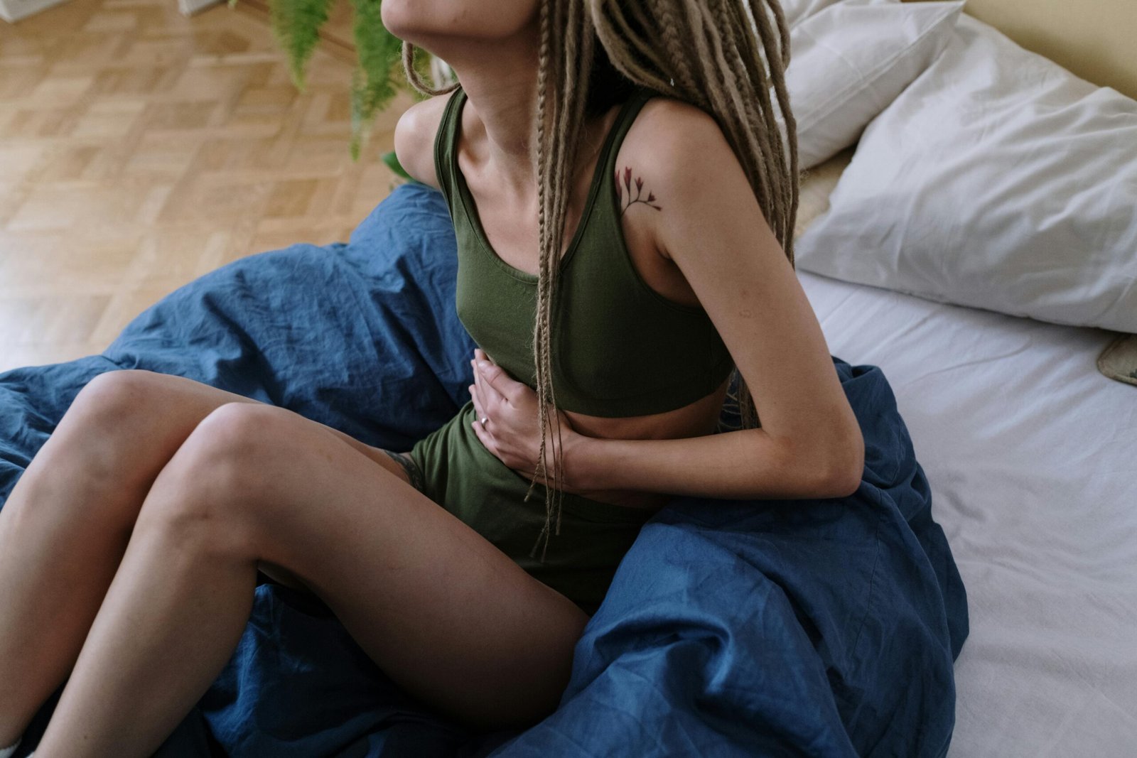 pexels-photo-6542682-6542682 Woman sitting in bed holding her stomach, indicating pain or discomfort, possibly due to cramps.