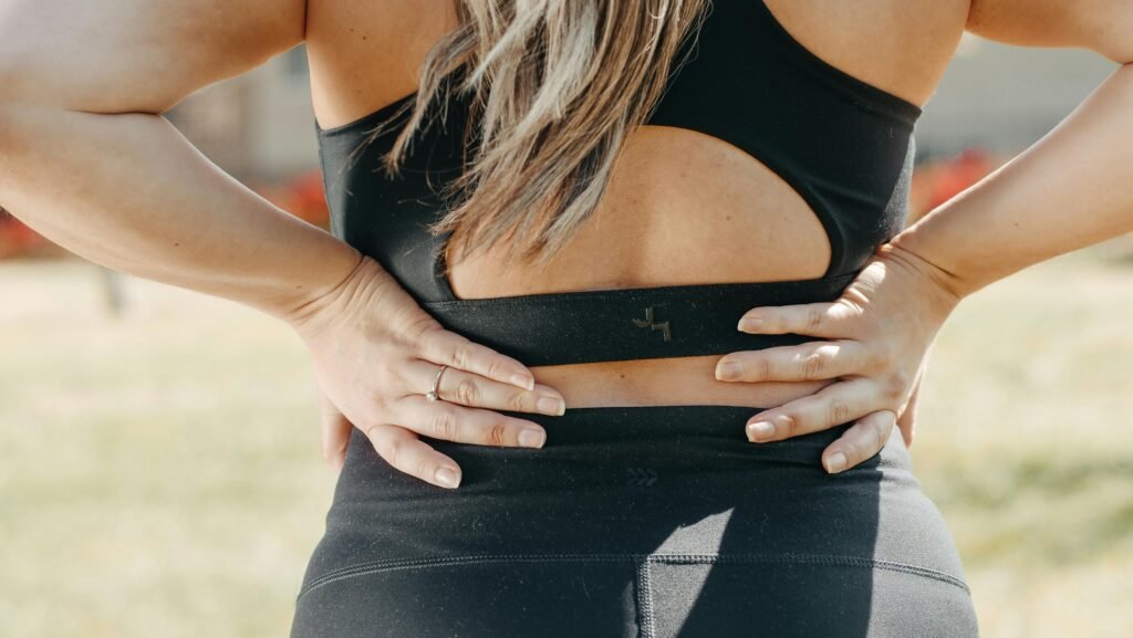 pexels-photo-7298412-7298412 A woman in activewear holds her lower back, indicating muscle strain, outdoors.